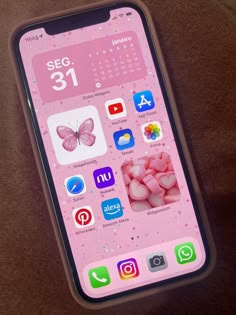 an iphone with pink and white icons on the screen, sitting on a brown surface