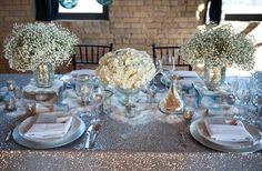 the table is set with silver sequins and white flowers