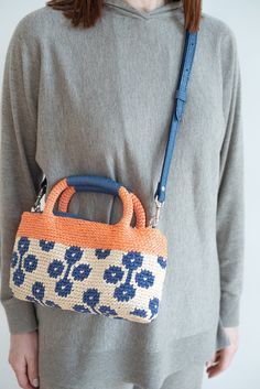 a woman wearing grey sweater holding an orange and blue handbag with flowers on it