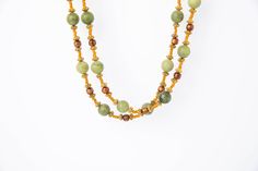 Weave your own history with the Green Jade Hanging. This stunning necklace is crafted of two long strands of matte green jade with gold coral, gold spacers and copper seed beads . Gold adjustable chain with lobster claw clasp. The gold tone chain and lobster claw clasp can be adjusted to your preferred length and worn as a choker or longer. It is also perfect for wearing in parties, wedding ceremonies and other formal occasions. Green Multi-strand Wooden Beads Jewelry, Elegant Green Beaded Necklaces With Wooden Beads, Elegant Green Beaded Necklace With Wooden Beads, Elegant Green Wooden Beaded Necklaces, Green Multi-strand Hand-strung Necklaces, Handmade Gold Jade Beaded Necklaces, Gold Double Strand Hand-strung Beaded Necklaces, Matte Green, Murano Glass Beads