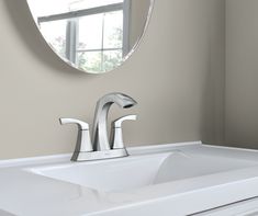 a bathroom sink under a round mirror in front of a wall mounted faucet