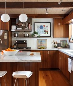 a kitchen with wooden cabinets and white counter tops, two stools are in front of the island