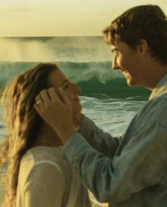 a man and woman standing next to each other in front of the ocean with waves