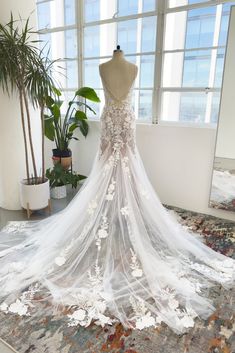 the back of a wedding dress on display in a room with large windows and potted plants