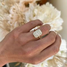 a woman's hand with a diamond ring on her finger and flowers in the background