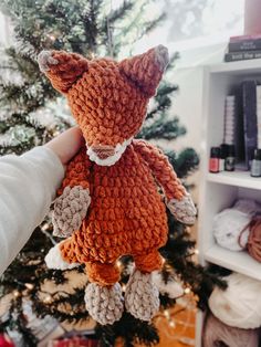 a hand holding a small stuffed animal in front of a christmas tree with yarn balls