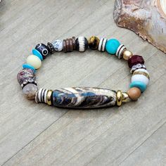 This bracelet is composed with an array of different beads. The main focal bead is a Tibetan hand painted stone bead in browns, cream, a hint of turquoise and red. It complements the other assorted gemstones and bone beads in this bracelet, One of a kind! Assorted gemstones Assorted ethically sourced bone beads Assorted glass beads Assortment of wood, shell, and brass with rhinestones Strong stretch cord Fits a wrist up to 6.75" Created in studio - Wilmington, NC Diy Bracelet Designs, Painted Stone, Hand Painted Stones, Natural Stone Bracelets, Wilmington Nc, Bone Beads, Bead Bracelets, Diy Bracelet, Focal Bead