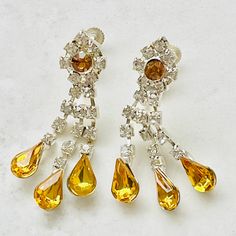 Stunning pair of 1950s silvertone crystal earrings. These fabulous vintage drop earrings feature three strands of beautiful clear crystal rhinestones. Each strand of crystals supports a lovely teardrop shaped citrine coloured glass rhinestone. The earrings have a hinged screw back fastening and all the stones are set in a silver tone thermo setting. These genuine vintage earrings are in almost perfect condition with only small signs of their age on the reverse. The perfect finishing touch to any outfit and a wonderful gift for a birthday, anniversary or as the something old for the bride to be. Measurements: Length: 4.5cm Width at widest point: 1.5cm Your vintage earrings will be wrapped in a piece of fabric with a satin ribbon and a brand tag. Crystal Wedding Jewelry, Vintage Drop Earrings, Coloured Glass, Wedding Jewellery, Almost Perfect, Crystal Wedding, Small Signs, Screw Back Earrings, Birthday Anniversary