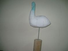 a white stuffed bird sitting on top of a wooden pole in front of a wall