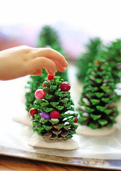 small pine cone trees on a tray with one being held over the other by someone's hand