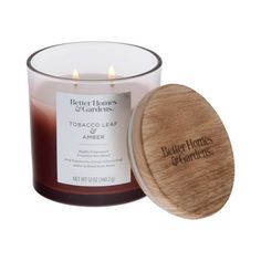 a glass candle with a wooden lid next to an empty container that says better homes candles