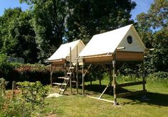 three tents are set up in the grass with ladders on each side and one has a birdhouse attached to it