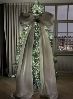 a white christmas tree with lights in front of it and a large bow on the top