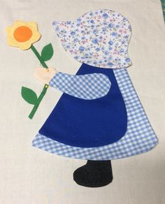 a paper doll holding a flower on top of a white cloth covered table with blue gingham