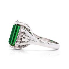 This is a fine piece of jewelry carefully crafted to perfection. This GIA certified 11.22 CT emerald-cut green tourmaline, is set on a platinum 900 band. The 10 0.25 CTTW prong set round-cut diamonds, enhance the gemstones rich green color. Some consider this precious stone to be symbolic of growth and harmony. The ring in its totality weighs 8.70 grams.   Details:  Item Type: Ring Metal: Platinum 900  Size: 6.75 (adjustable)  Weight: 8.79 grams  Setting: Prong, Filigree  Stone Details:  Gemstone: Green tourmaline Carat: 11.22 CTTW Color: Green Cut: Emerald Transparency: Transparent Measurements: 14.09 x 11.06 x 6.96 mm  GIA Report Number: 1499048026  Side Stone Details: 10 round cut diamonds, 0.25 CTTW, prong setting Gia Certified Tourmaline Rings For Formal Occasions, Green Octagon Platinum Ring, Luxury Green Tourmaline Emerald Ring, Green Platinum Emerald Ring For May Birthstone, Platinum Baguette Cut Green Emerald Ring, Formal Platinum Emerald Ring May Birthstone, Formal Platinum Emerald Ring For May Birthstone, Elegant Polished Emerald Cut Emerald Ring, Formal Tourmaline Ring With Baguette Cut