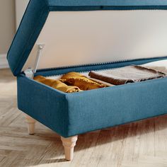 a blue ottoman bed with an open lid on the bottom and two blankets in it