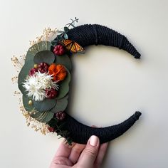 a hand holding a fake flower wreath on top of a white surface with an elephant's nose