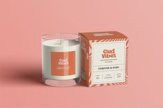 a white candle sitting next to a box on a pink background with the words gud vibes printed on it