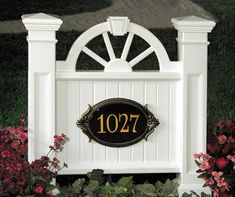 a white gate with a black address sign and flowers in the foreground on a sunny day