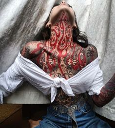 a woman with tattoos on her body and chest sitting in front of a white sheet