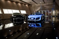 three cars are parked in a showroom with reflective flooring and lighting on the walls