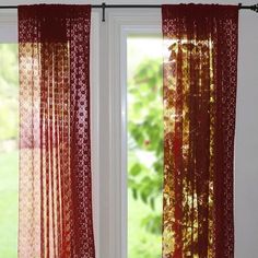 two red sheer curtains hanging on a window sill in front of a green yard