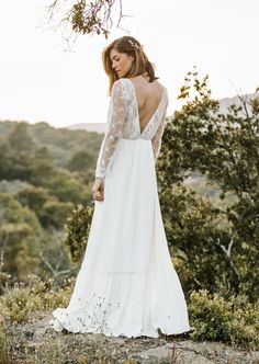 a woman standing on top of a hill wearing a white dress and holding her back to the camera