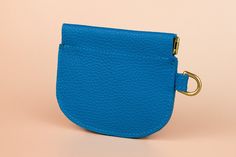 a small blue purse with a gold ring on the front and bottom, sitting on a pink background