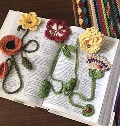 an open book with crocheted flowers on it sitting on top of a table