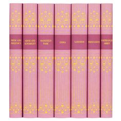 six pink books with gold lettering on the front and back covers, all lined up in rows