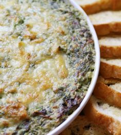 a white bowl filled with spinach dip surrounded by slices of bread