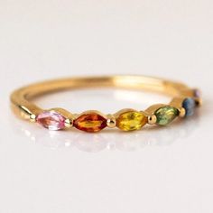 a yellow gold ring with multicolored stones on the side, sitting on a white surface