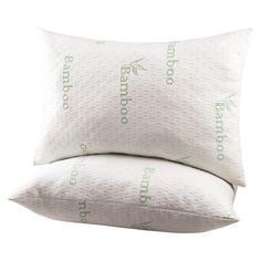 two pillows sitting next to each other on top of a white pillow case with green lettering