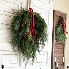 a wreath hanging from the side of a door with pine cones and greenery on it