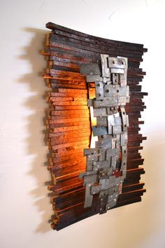 a sculpture made out of metal and wood on a white wall next to a lamp