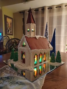 a house made out of icing on top of a wooden table next to a christmas tree