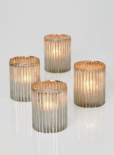 three glass candle holders sitting next to each other on a white surface with light coming from them