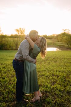 a man and woman kissing in front of a pond on a sunny day at sunset