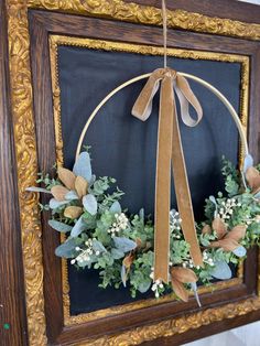 a wreath is hanging on a frame with ribbon and greenery in front of it