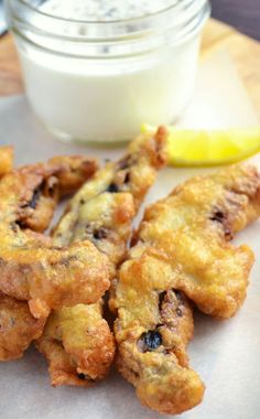 some fried food on a plate next to a glass of milk and lemon wedges