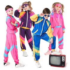 three girls in colorful clothing standing next to each other with a tv on the ground