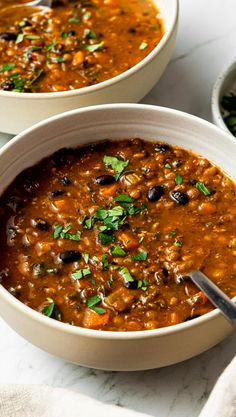 two bowls filled with soup on top of a white table next to another bowl full of food