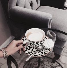 a person is holding a coffee cup and saucer with whipped cream in it on a chair