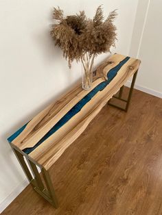 a wooden bench sitting on top of a hard wood floor next to a vase filled with dry grass