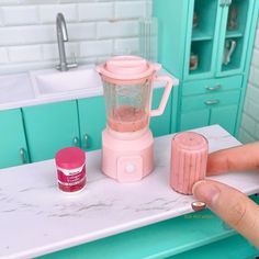 a person holding a pink blender on top of a counter next to a sink