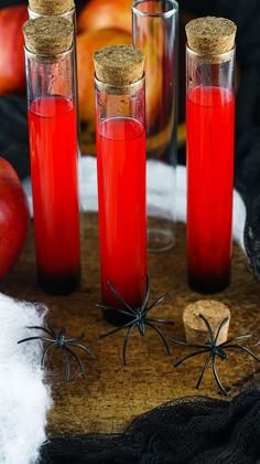 three bottles filled with red liquid sitting on top of a wooden table next to apples