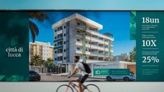 a man riding a bike in front of a large advertisement for an apartment building on the street