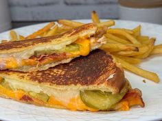 two grilled sandwiches with cheese and pickles on a plate next to french fries