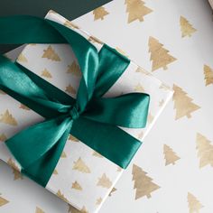 a present wrapped in white and gold paper with a green bow on it's side