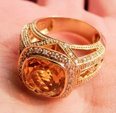 a close up of a person's hand holding an orange ring with diamonds on it